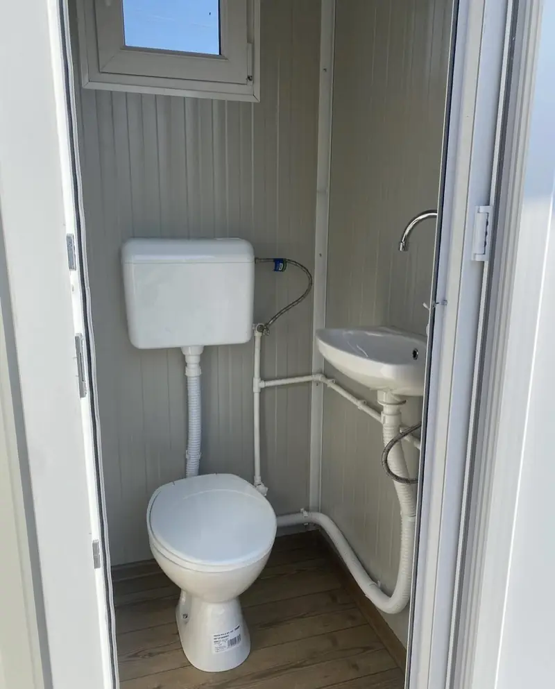 Inside a single-stall flushing restroom with tank toilet and small sink