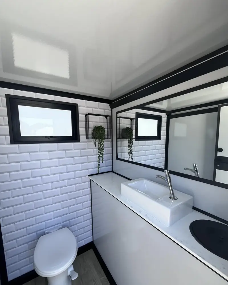 Restroom trailer interior with flushing toilet, vessel sink, mirror and window