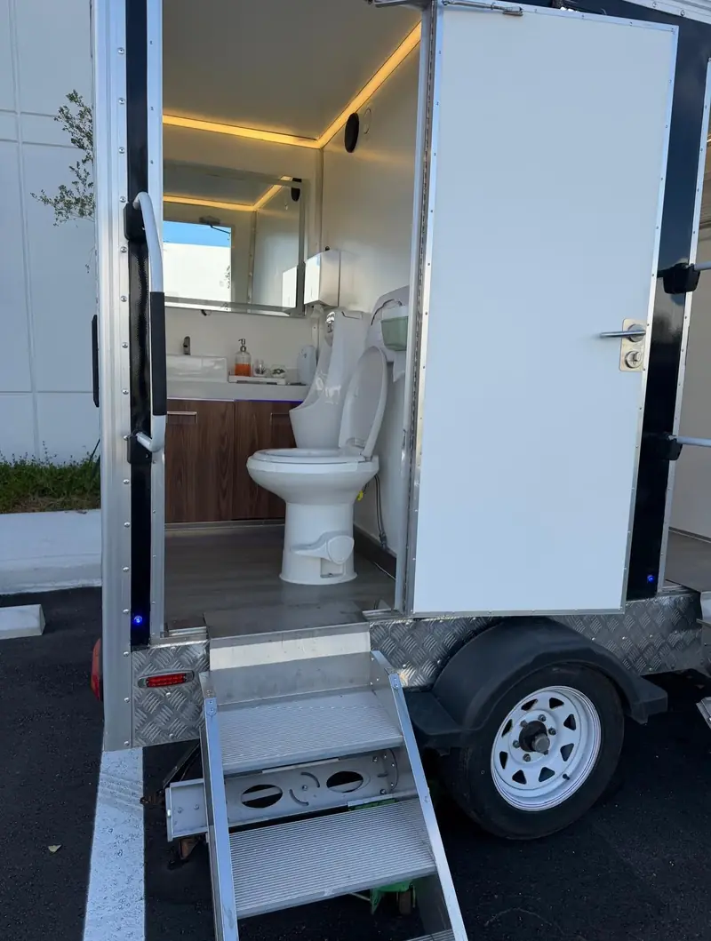 Restroom trailer stall with door open showing a flushing toilet and vanity