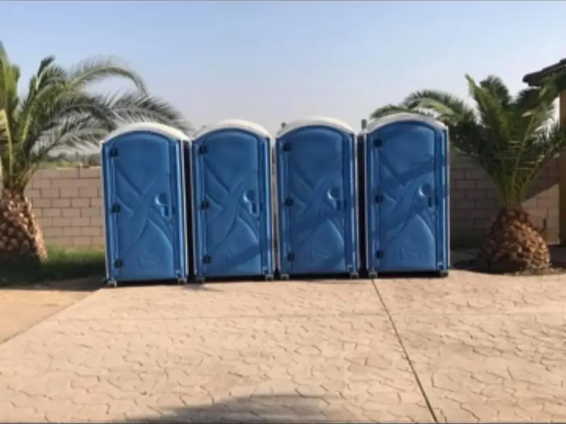 Four blue standard porta potties lined up on a concrete lot