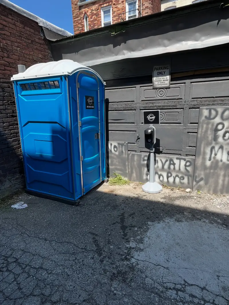 Blue standard porta potty placed on a paved driveway beside a garage