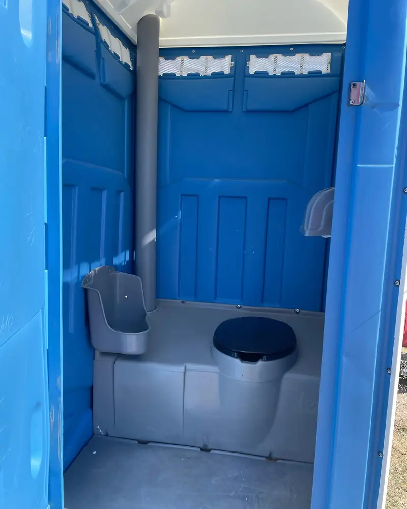 Interior of a blue standard porta potty with toilet, urinal and toilet paper holder